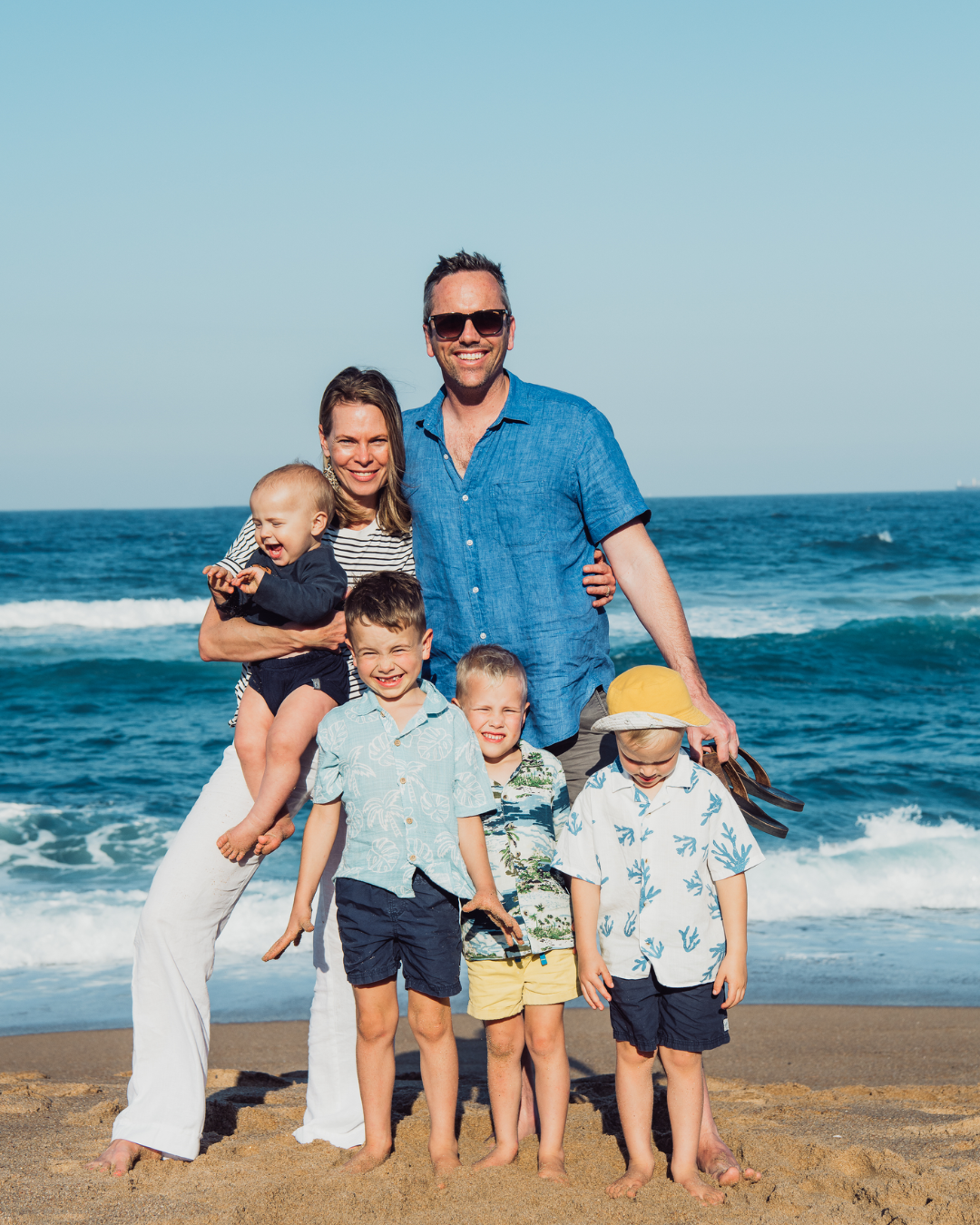 Family of six posing on a beach with ocean waves in the background